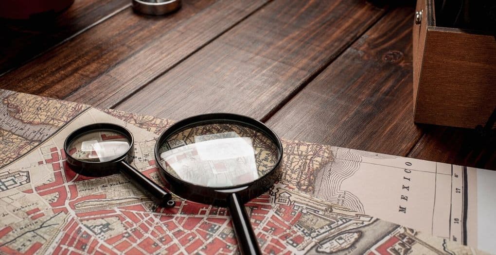 A magnifying glass and a map on a wooden table - tools for exploring and navigating. They imply that someone is searching for a place on the map.