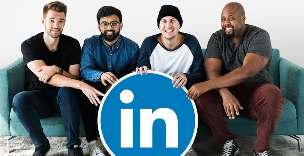 Four people are sitting on a sofa, holding a LinkedIn logo together in front of them.