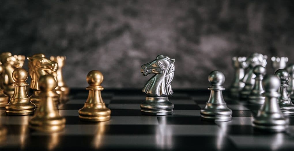 Gold and silver chess pieces on black and white chess board, symbolizing strategic playing.