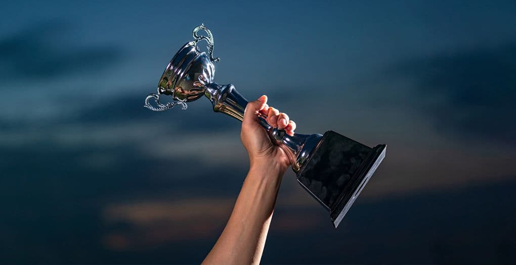 A person triumphantly holds up a trophy against a dark sky, symbolizing victory and achievement.