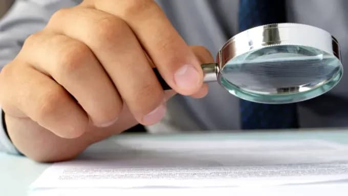 A person closely inspecting a document using a magnifying glass.